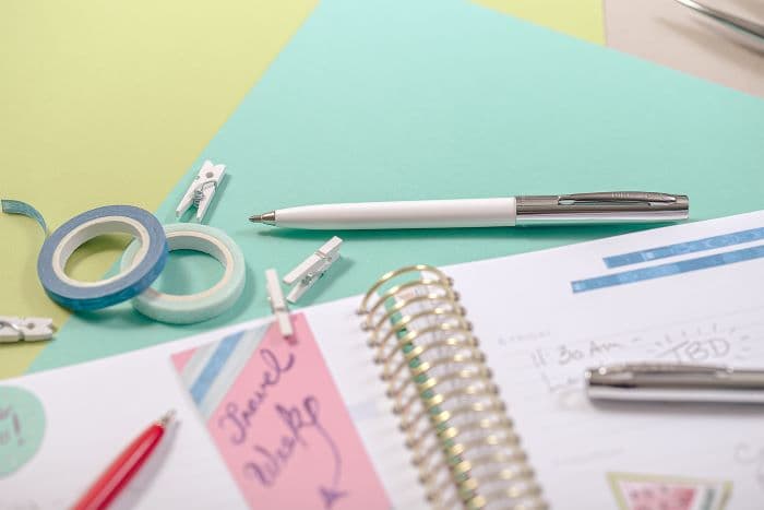 White and Red cap-o-matic space pens with chrome accents laying atop a lined, spiral planner.