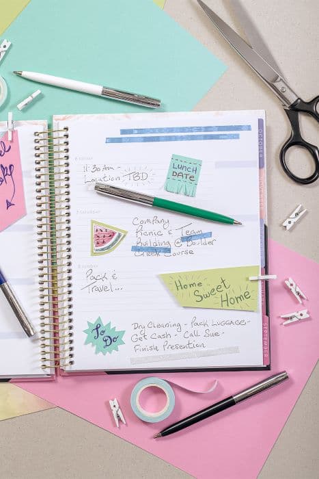 White, Green, and Black cap-o-matic space pens with chrome accents laying atop a lined, spiral planner.