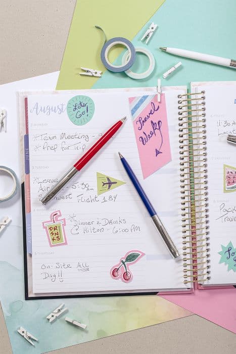 White, Red, and Blue cap-o-matic space pens with chrome accents laying atop a lined, spiral planner.