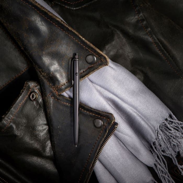AG7-BTN Dark Matter Astronaut Space Pen in black titanium nitride laying atop the lapel of a leather jacket and a silver knit scarf with fringe.
