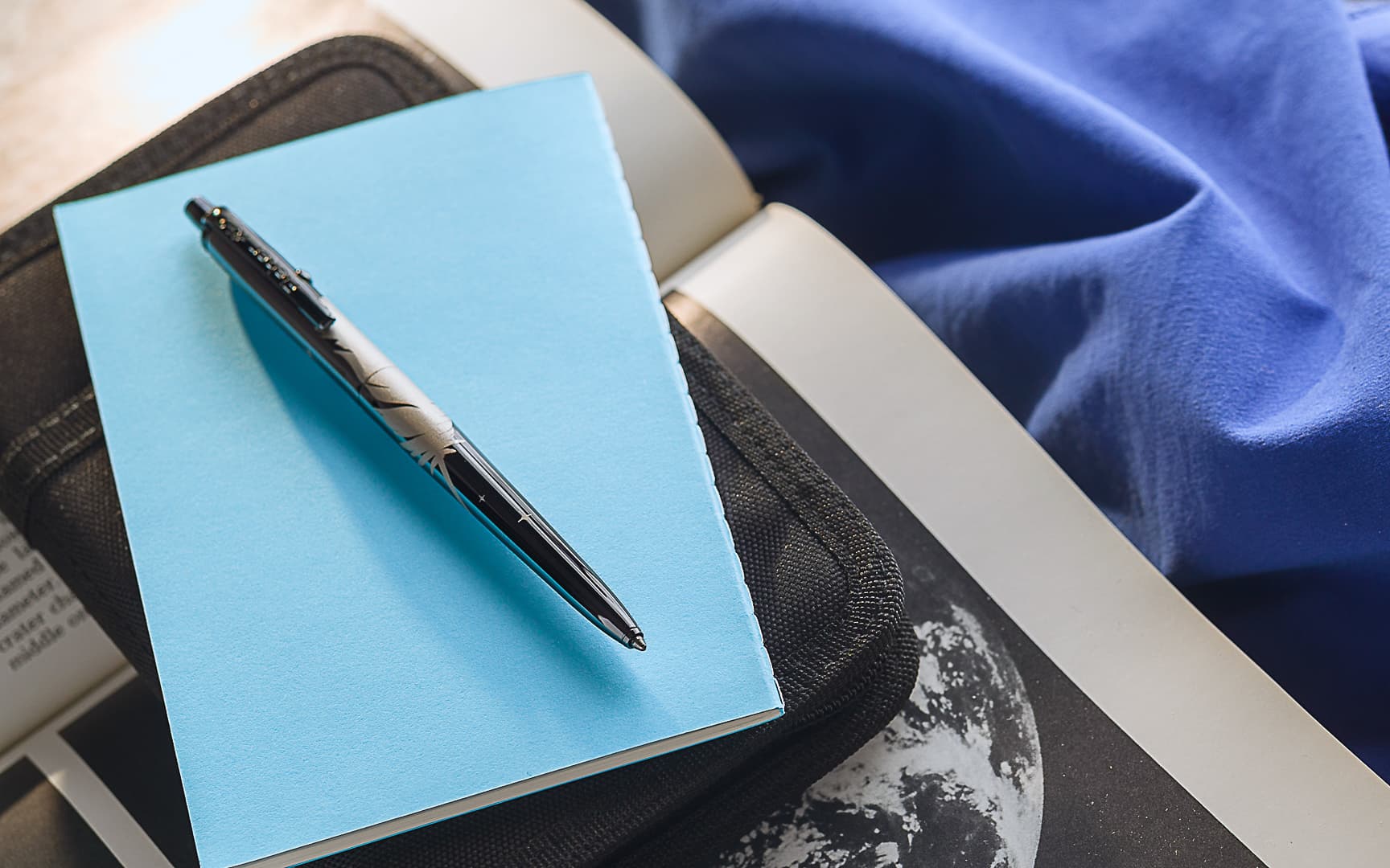 AG7-BTN/FS-BO Dark Matter Black Titanium Nitride Astronaut Space Pen, Blue Origin Special Edition laying atop a blue notebook.