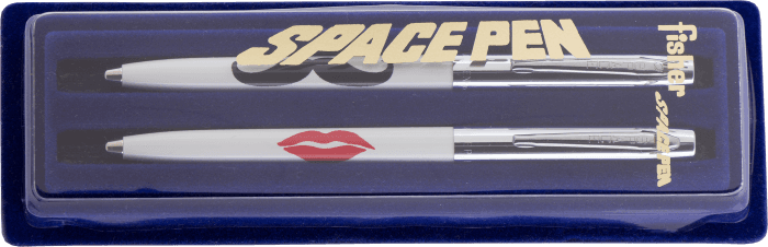 Cap-o-matic space pens with white plastic barrels, chrome caps, clips, and tips in a blue gift box. One pen is imprinted with a black mustache; the other is imprinted with a red kiss. The lid of the box says Space Pen.